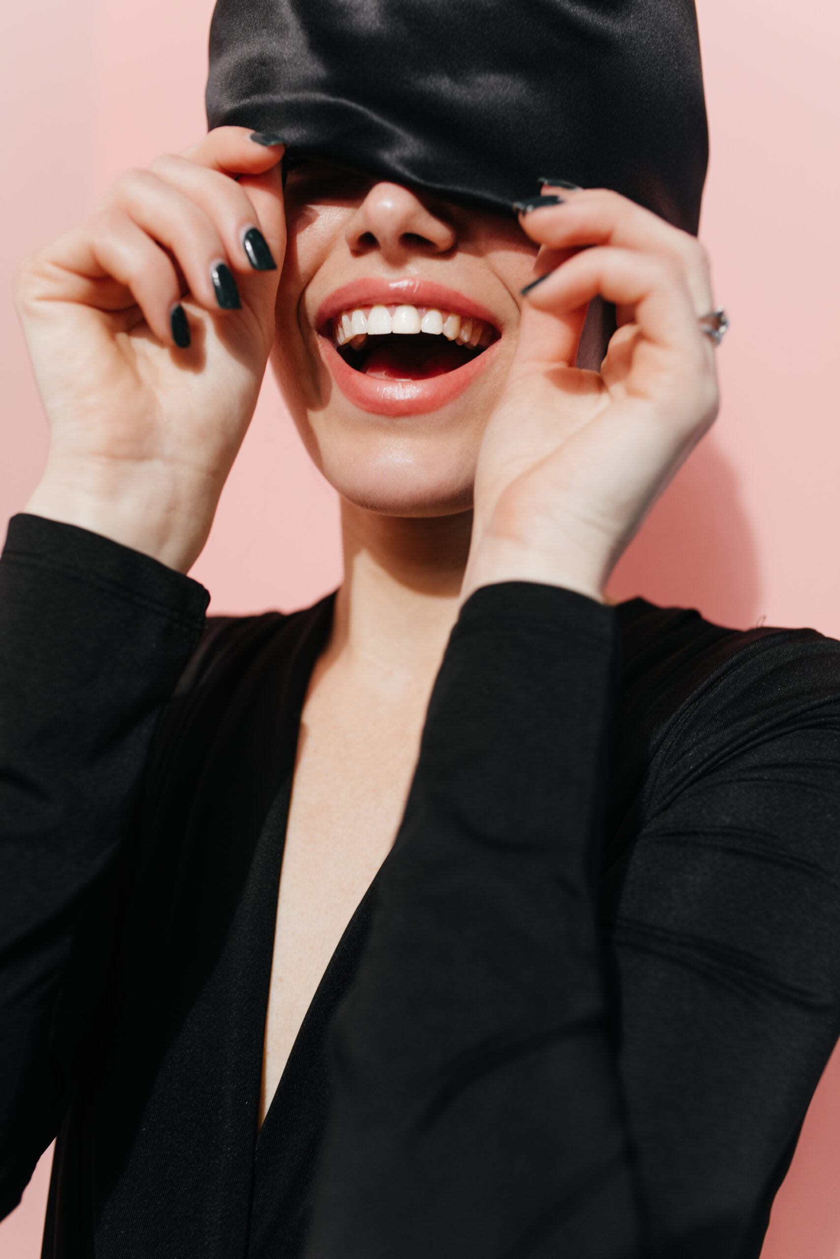 Blisful girl posing with trendy black head scarf. Studio shot of positive female model in turban laughing on pink background.